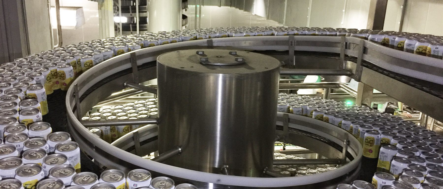 Beverage cans accumulating in large numbers on a spiral conveyor inside a canning plant.