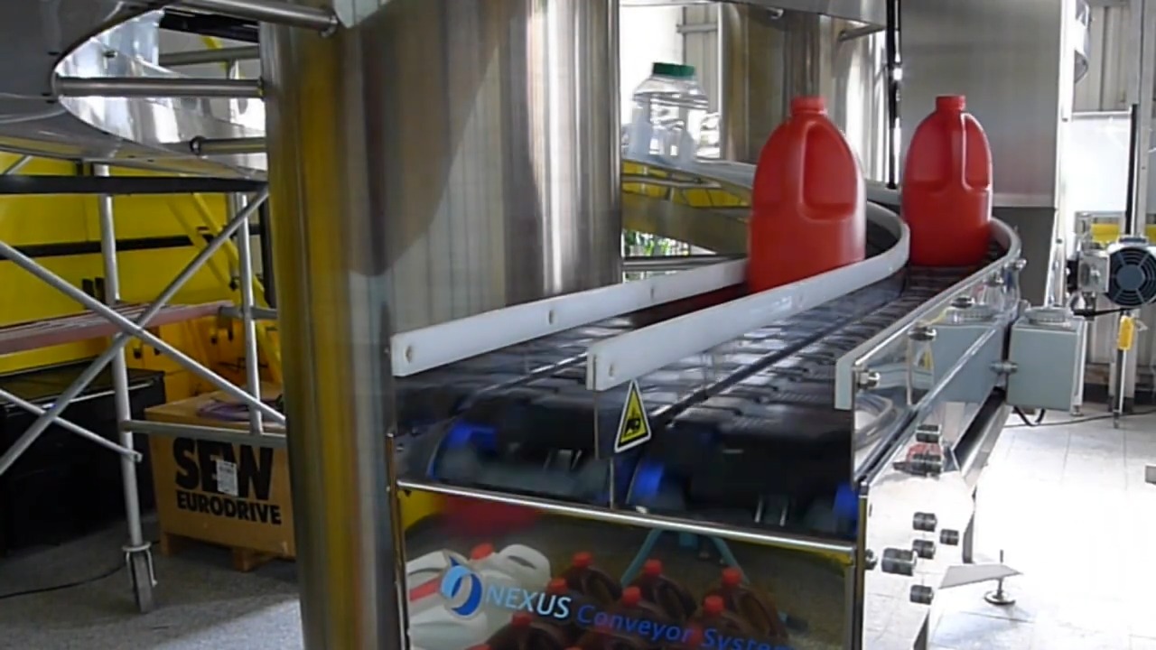 Two red plastic jugs on the two separate tracks at the outlet of a dual track spiral conveyor, divided by white guide rails.