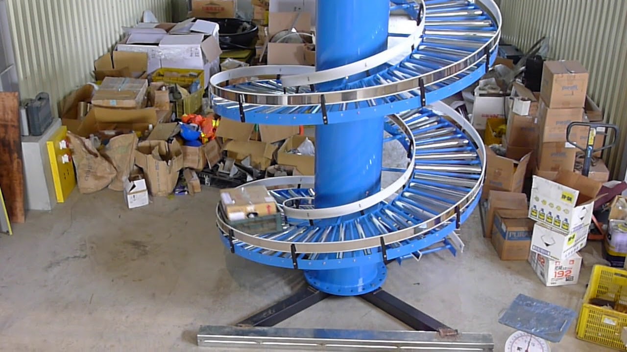 A gravity roller spiral conveyor with a blue column beside stacks of cartons.