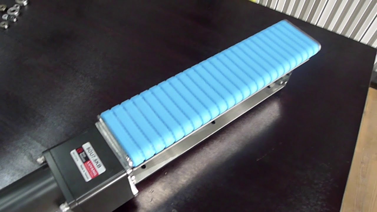 A short miniature conveyor with a blue modular belt and its motor, on a workbench.