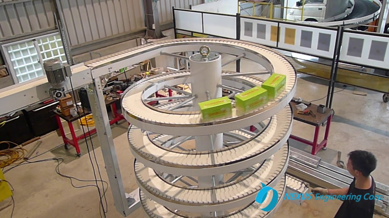 Green boxes on the narrow track of a white spiral conveyor in the NEXUS factory.