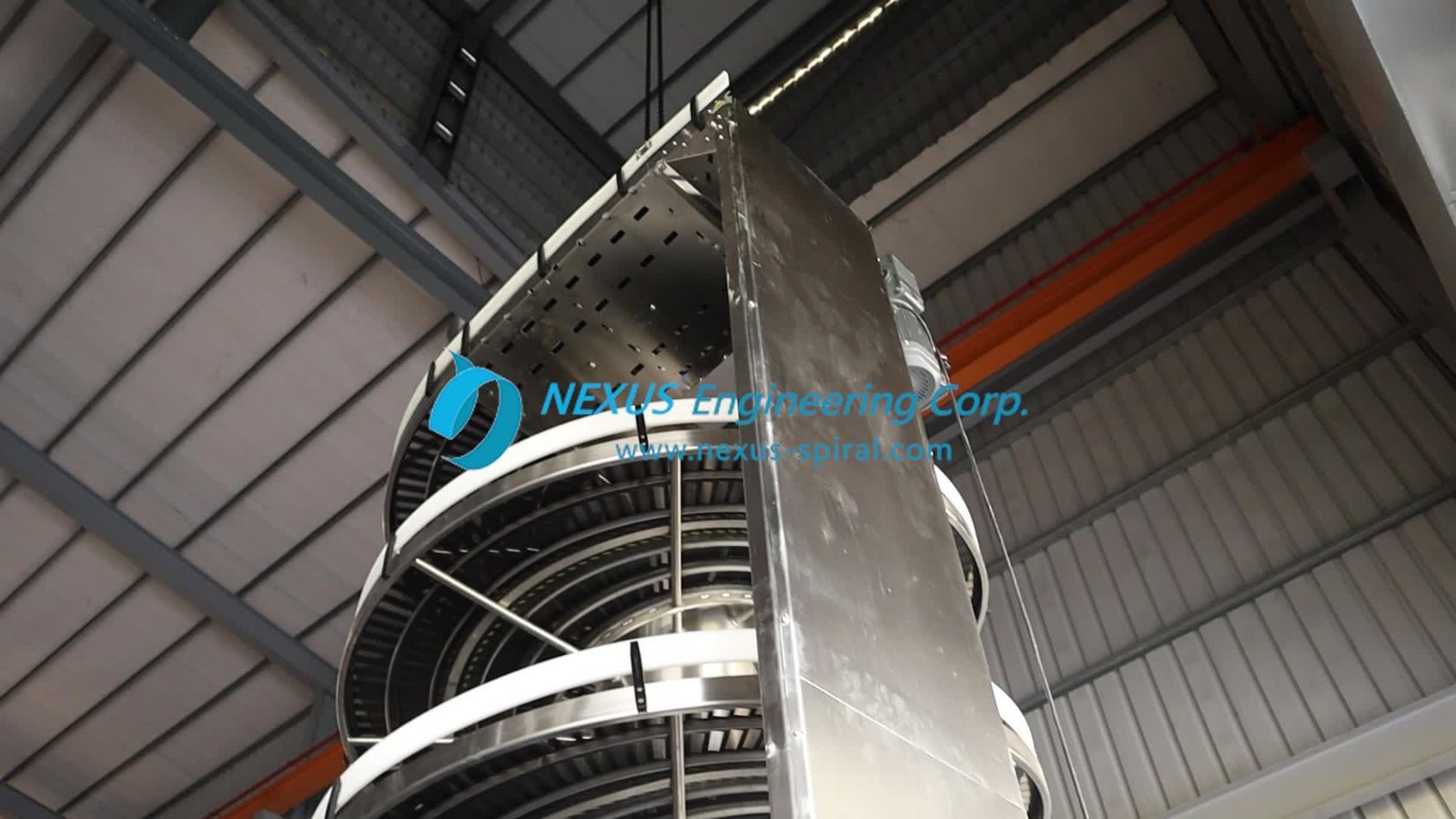 A stainless steel spiral conveyor seen from below in a factory building, its tiers wound around a central column.