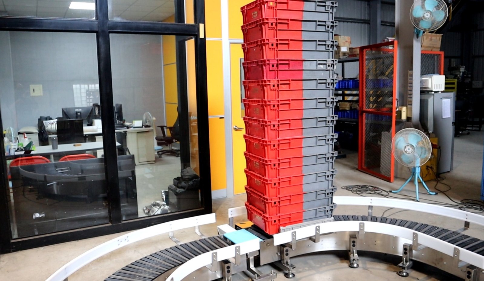 A tall stack of red plastic crates standing on the conveying surface of the curve conveyor in the NEXUS factory.