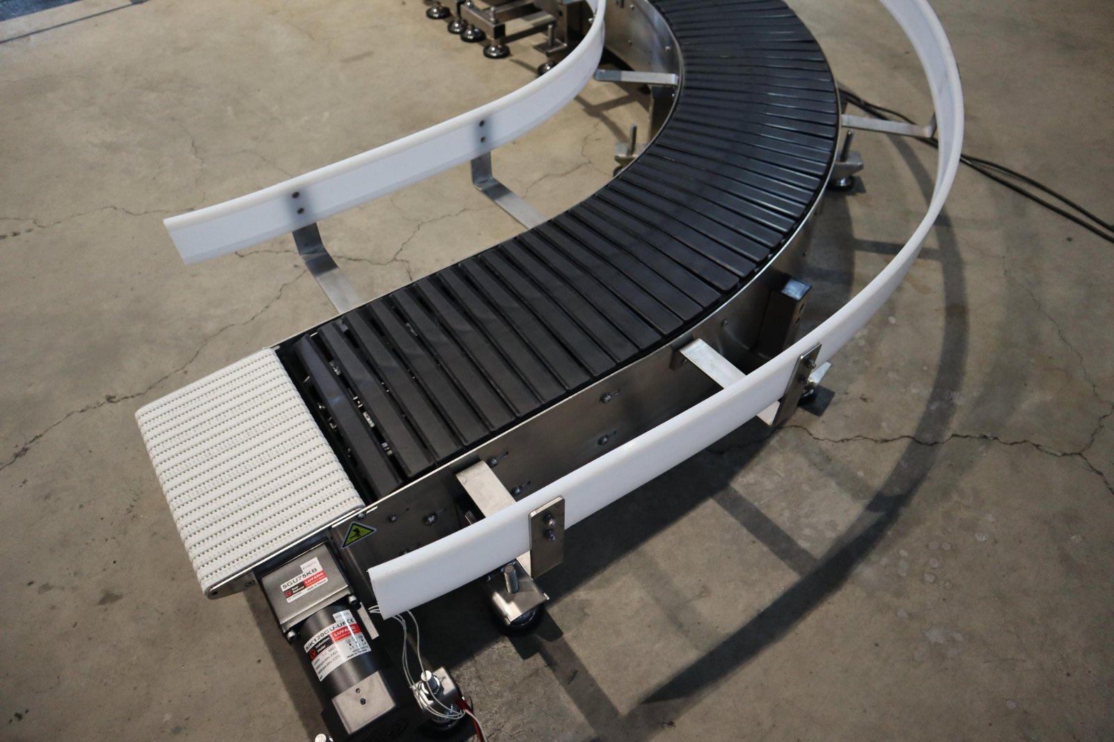 Close view of the point where the dark curved conveying surface meets the pale straight section on a single conveyor frame.