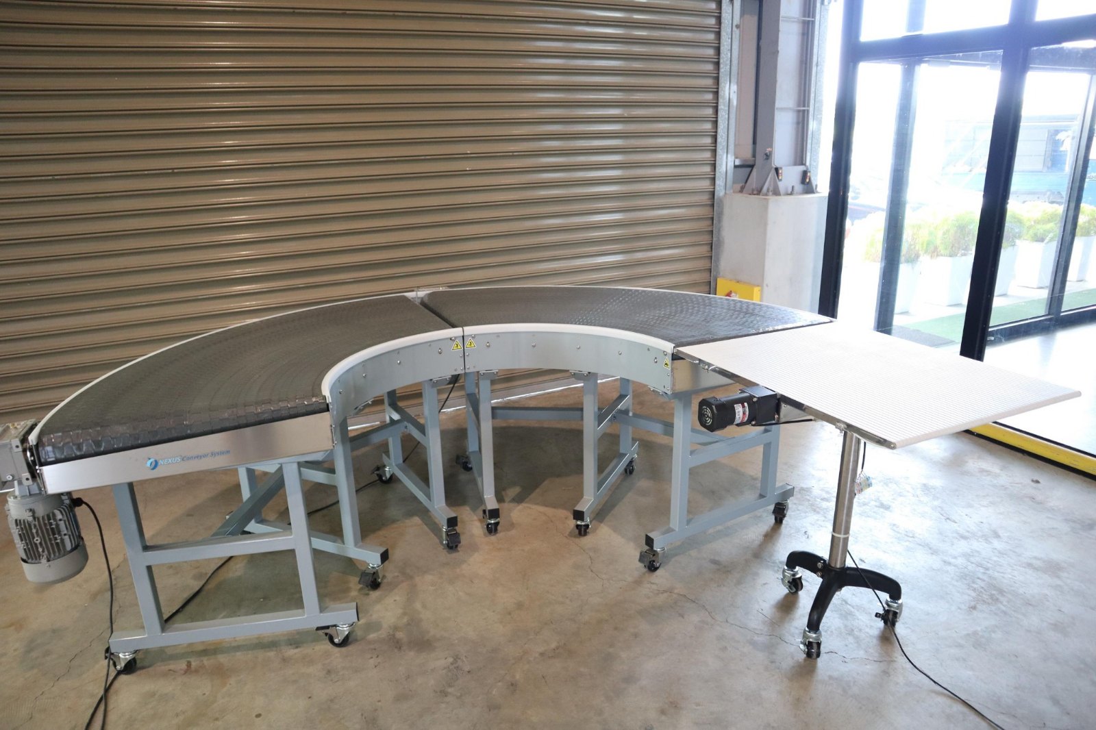 A complete curve conveyor on castors in the NEXUS factory, with a straight infeed section connected at one end.