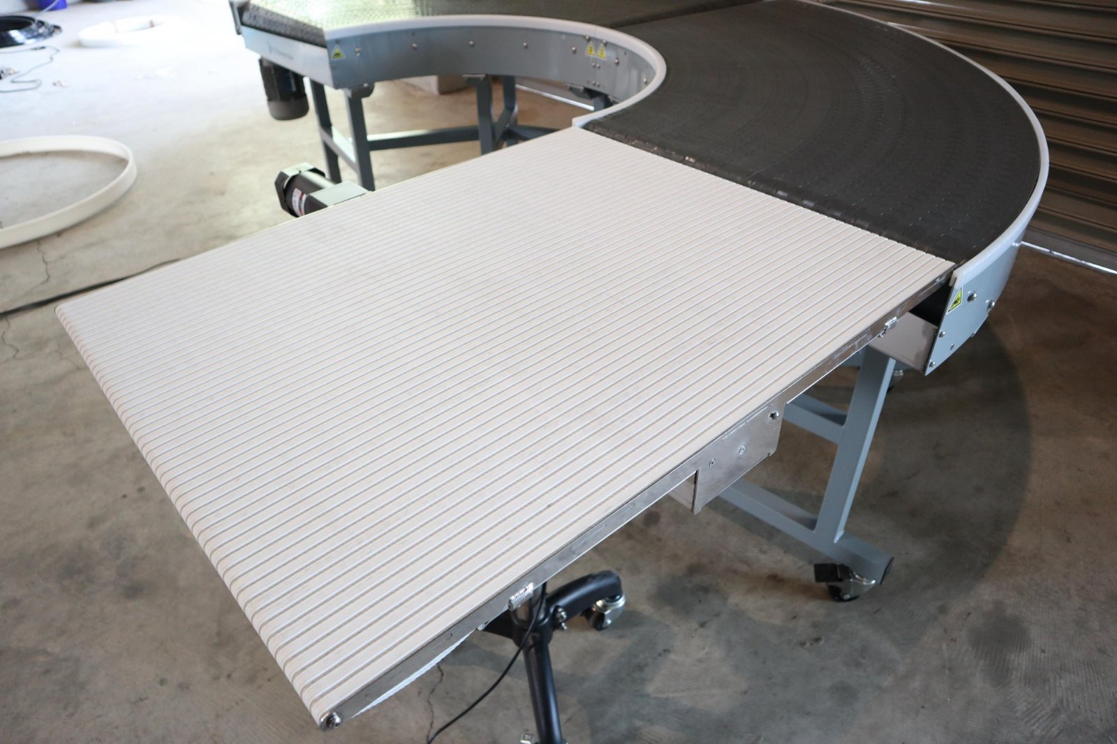 A curve conveyor photographed along the line of the turn, with a pale straight section running away from the curve.
