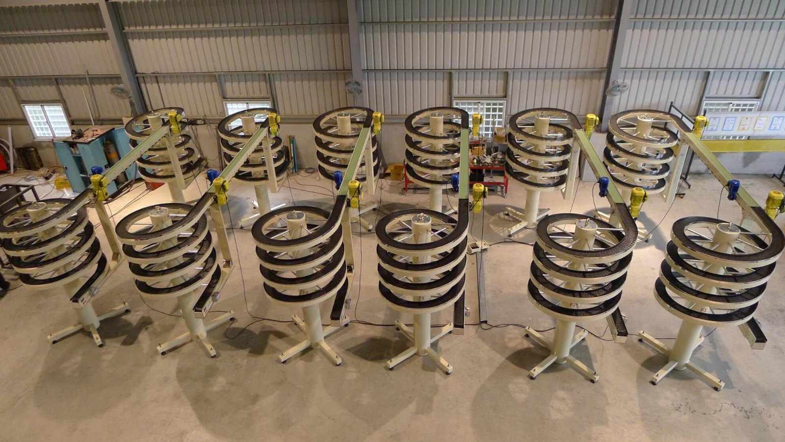A row of narrow track spiral conveyors standing side by side on the NEXUS factory floor, each wound around its own column.