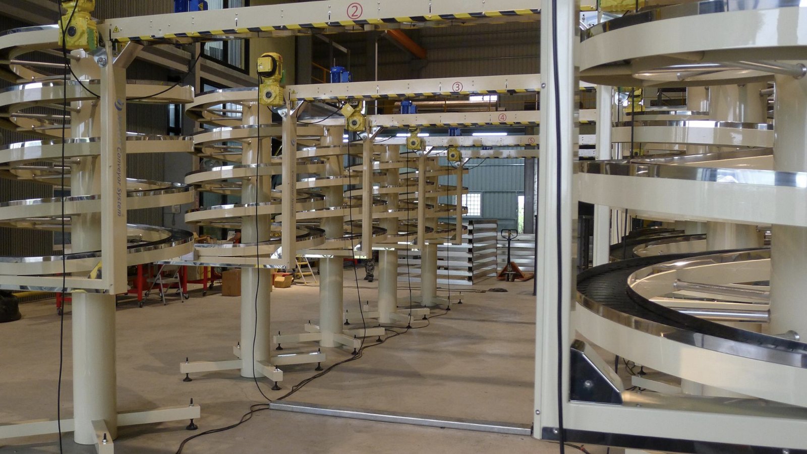A narrow track spiral conveyor seen at full height in the factory, its track wound in tiers around a central column.